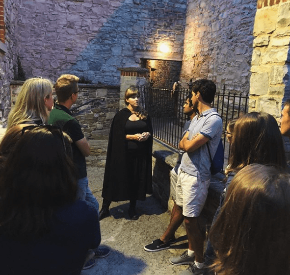 A tour guide wearing all black telling a story to a group in a limestone room
